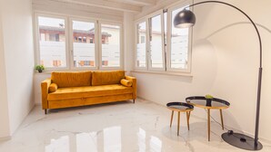 A room with a yellow sofa, two small round tables, a floor lamp, and large windows with a view of buildings outside. - Residence Piccolo Lord 2 - Italian Homing (Calcinato)