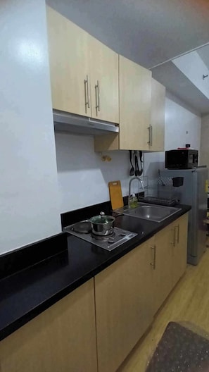 A kitchen with light wooden cabinets, a black countertop, a stove, a sink, and a refrigerator.