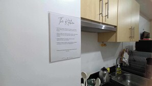 Une cuisine avec des meubles de rangement en bois, un évier en acier inoxydable et un panneau fixé au mur indiquant les consignes de nettoyage.