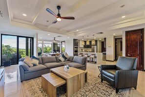 Un vaste espace de vie comprenant un canapé, une table basse et un fauteuil, un ventilateur de plafond et une vue sur l’extérieur.