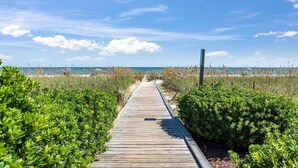 Ein hölzerner Steg führt zu einem Strand bei blauem Himmel.