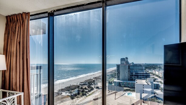 Ein Zimmer mit großem Fenster und Blick auf Strand und Stadt.