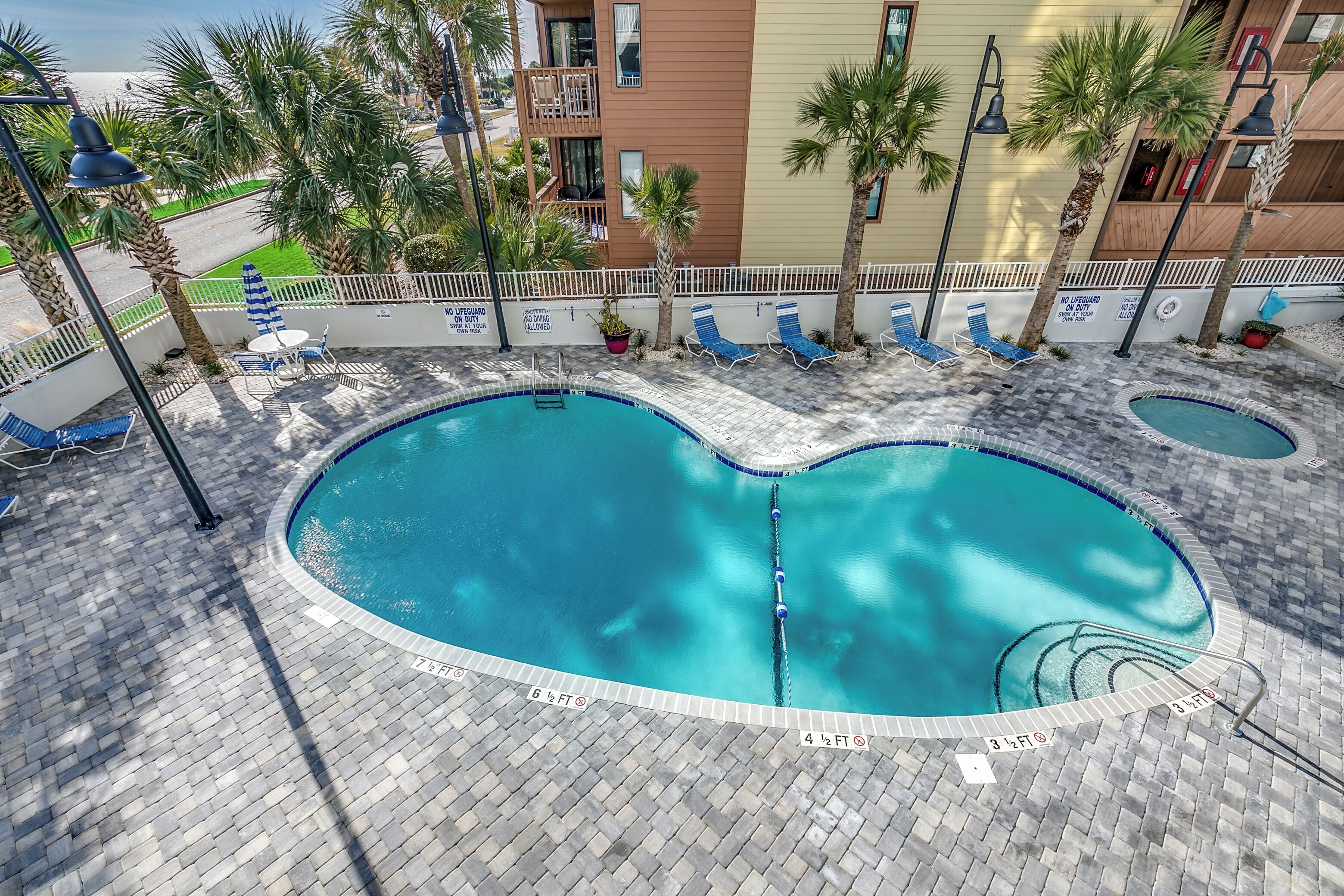 A swimming pool with a tiled deck, lounge chairs, and palm trees.
