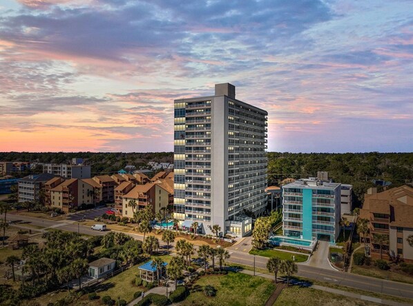 A high-rise hotel with multiple balconies, surrounded by other buildings and greenery.