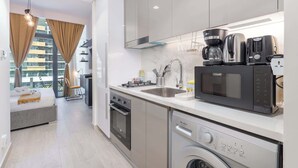 Cozinha moderna com forno embutido, micro-ondas e máquina de café. Há uma pia com torneira, e uma máquina de lavar roupa visível no canto.
