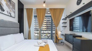 Quarto de hotel moderno com uma cama grande, televisão, escrivaninha e vista para a paisagem urbana através de janelas do chão ao teto.