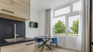 Eine moderne Küche mit schwarzer Arbeitsplatte, Holzschränken und einem Edelstahlspülbecken. Ein Essbereich mit rundem Tisch und zwei blauen Stühlen lädt zum Verweilen ein. Große Fenster bieten Blick ins Freie.
