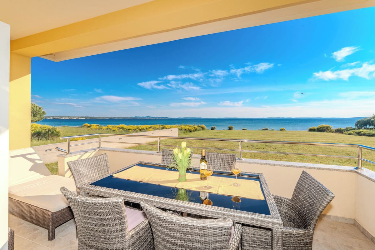 A balcony with a table and chairs, overlooking a coastal view.