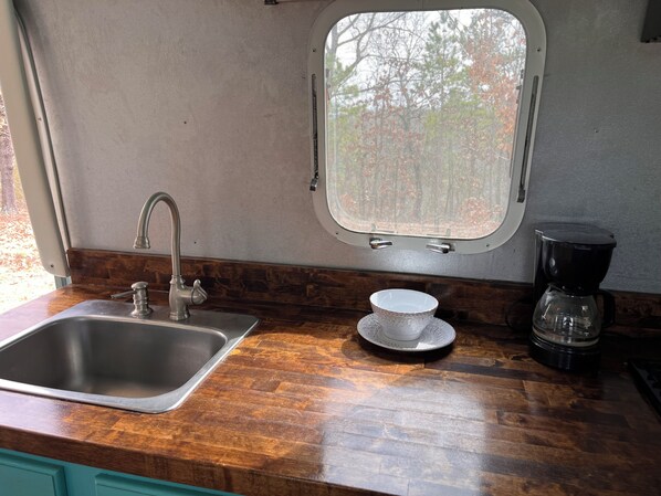 A kitchen with a stainless steel sink, a window, and a coffee maker.