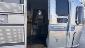 Una furgoneta camper vintage con la puerta abierta, mostrando una zona de cocina con estufa, sillas y una ventana.