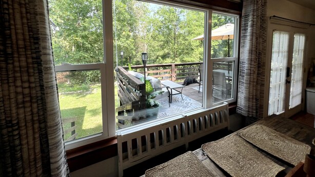 A room with large windows, a wooden deck, and a view of a garden. - Cozy Home - Fire Pit - Seasonal Fishing (Williford)