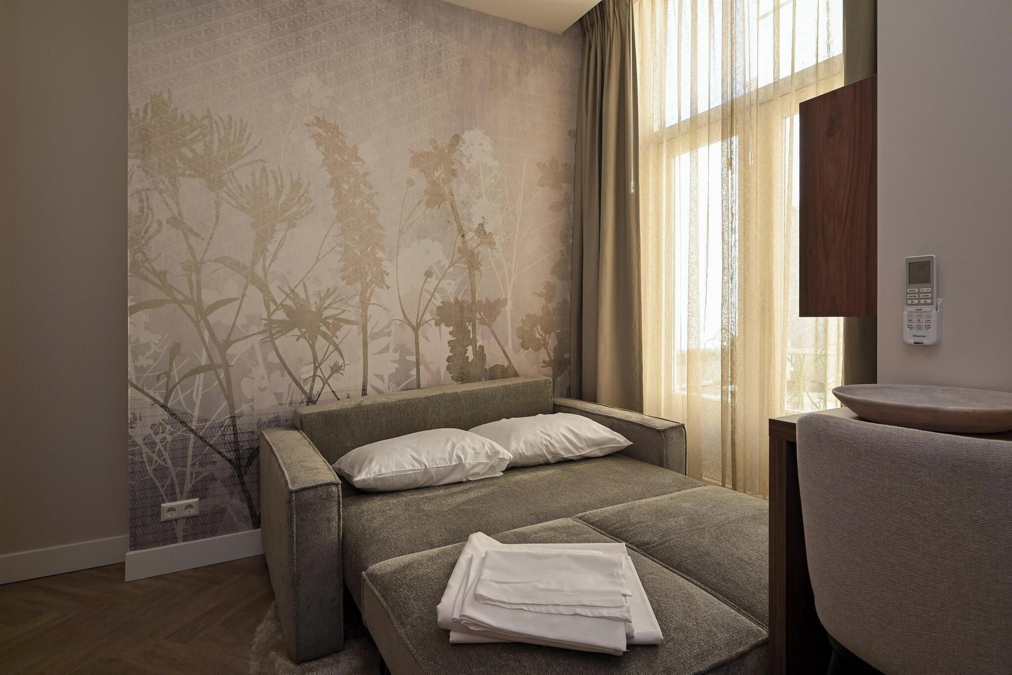 A modern bedroom with a bed, a chair, and a wall-mounted control panel.