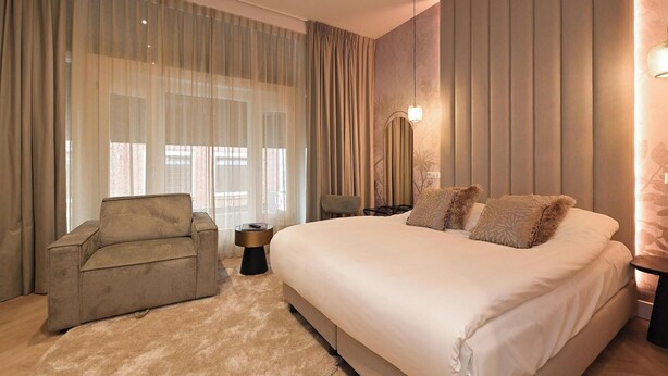 A bedroom with a large bed, a sofa, a side table, and a lamp. - Novallure Downtown (The Hague)