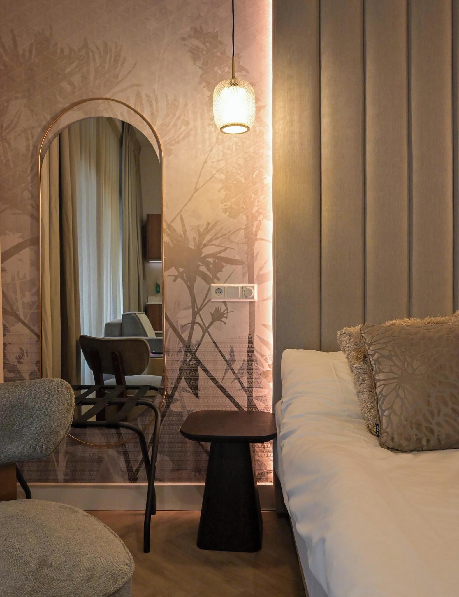 Una habitació d'hotel amb un llit, una taula petita, una cadira, un escriptori i un mirall.