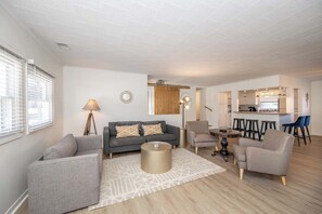 Una sala de estar moderna con un sofá, sillones, una mesa de centro y un comedor con taburetes.