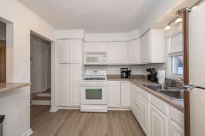 Una cocina moderna con armarios blancos, un lavamanos de acero inoxidable y un microondas.