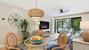 A modern living room with a glass dining table, wicker chairs, a large TV, and a view of the outdoors. - J-156 -Updated, Designer Furnished, With Lake Views (Naples)