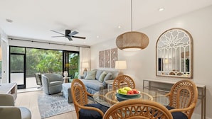 A modern living room with a glass dining table, wicker chairs, a grey sofa, and a large window with a view of greenery. - J-156 -Updated, Designer Furnished, With Lake Views (Naples)
