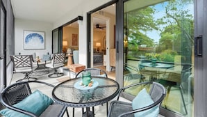 A modern outdoor patio with wicker furniture, a glass table, and a view of the garden. - J-156 -Updated, Designer Furnished, With Lake Views (Naples)