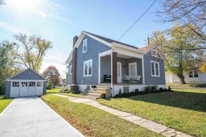 A two-story house with a front porch, a garage, and a well-maintained lawn. - Bridgetown Bungalow (Cincinnati)