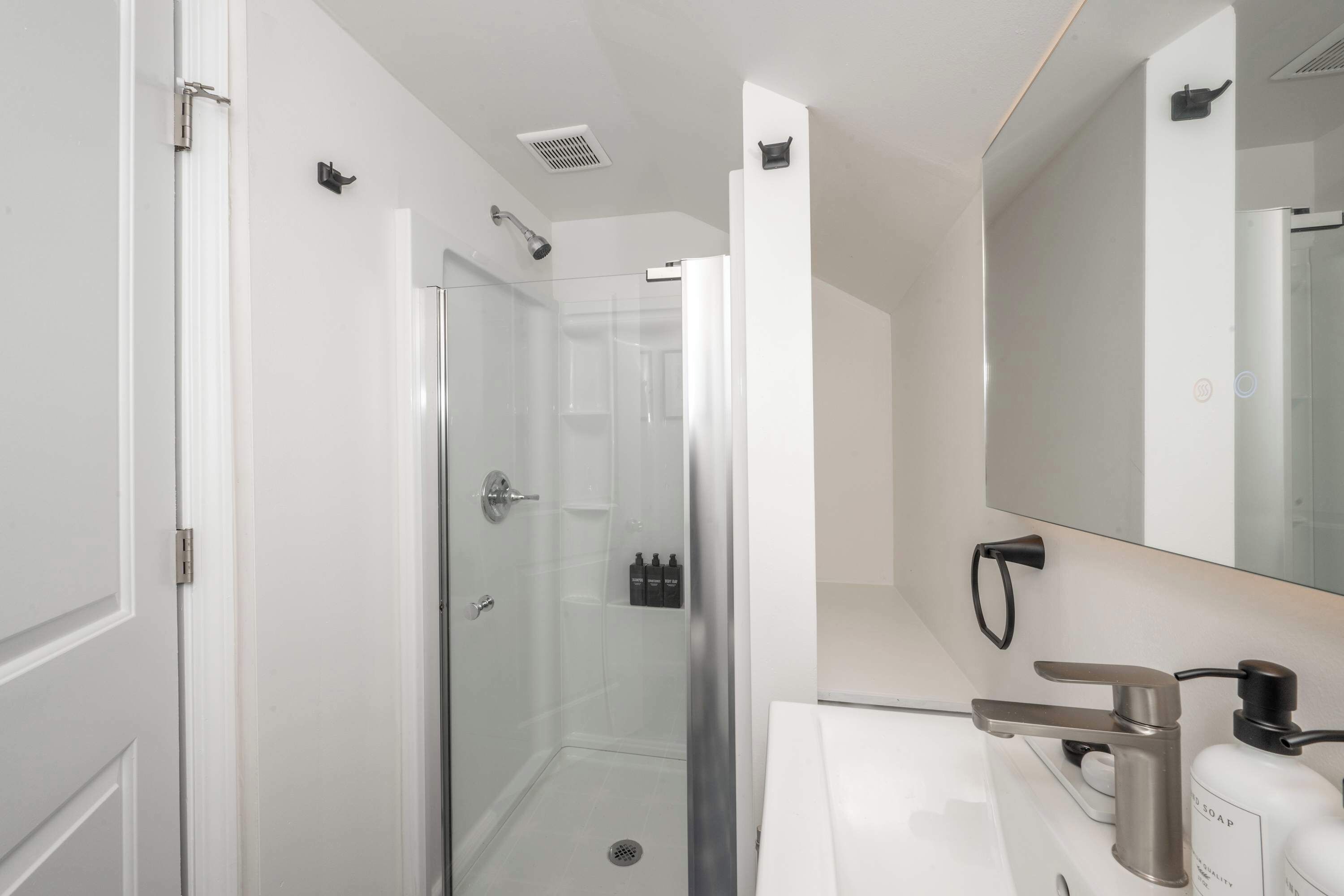A modern bathroom with a glass-enclosed shower, a white sink, and a large mirror.
