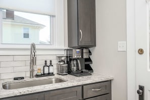 Una cocina con encimera de granito, cafetera y lavamanos.