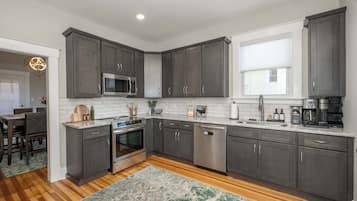 A modern kitchen with dark cabinets, stainless steel appliances, and a wooden floor.