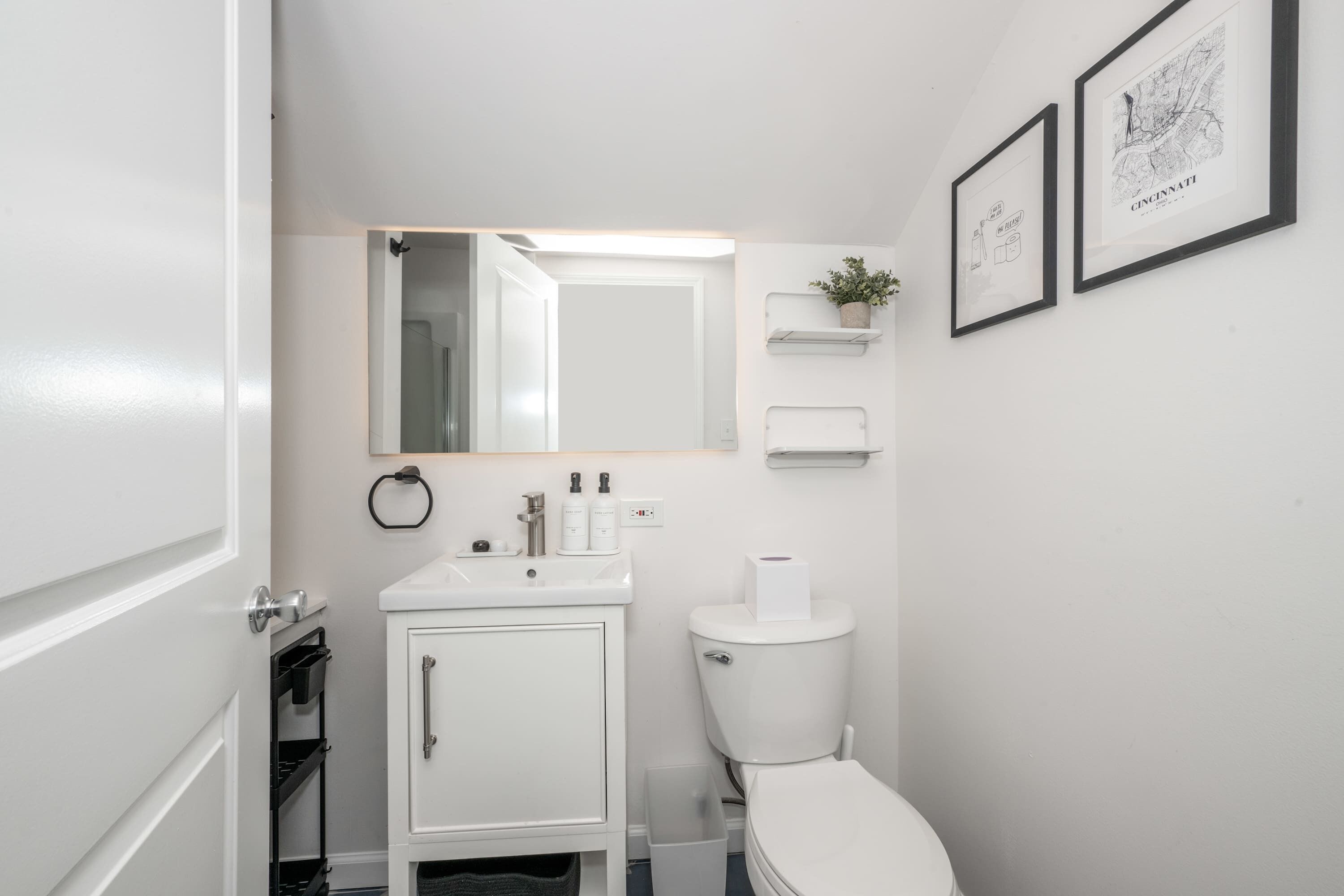 A modern bathroom with a white sink, toilet, and cabinet. There are framed maps on the wall.
