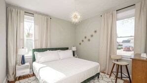 Un dormitorio moderno con una cama grande, mesitas de noche, un escritorio y vistas al exterior.
