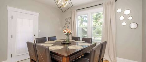 A dining room with a wooden table, six chairs, a vase with flowers, and a geometric pendant light.