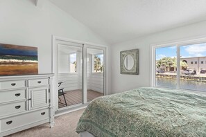 Ein Schlafzimmer mit Bett, Schminktisch, einem Gemälde, einem Spiegel und Blick auf einen Balkon und Wasser.