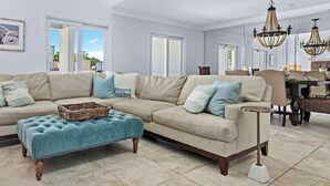 Ein geräumiges Wohnzimmer mit einem beigefarbenen Ecksofa, einem blauen Hocker und einer Pendelleuchte.