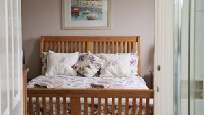 A bedroom with a wooden bed, floral bedding, and a framed painting of a harbor scene on the wall. - Town centre apartment with parking- Dog friendly! (Padstow)