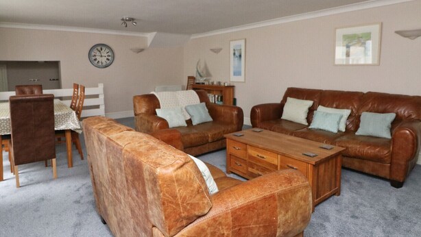 A living room with a brown leather sofa set, a wooden coffee table, and a dining area with a table and chairs. - Town centre apartment with parking- Dog friendly! (Padstow)