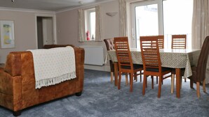 A cozy living room with a brown sofa, a dining table with wooden chairs, and a large window with curtains. - Town centre apartment with parking- Dog friendly! (Padstow)