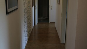 A hallway with wooden flooring, white walls, and framed pictures. There is a door at the end of the hallway. - Vacation apartment Molly (Brunsbüttel)