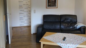 A living room with a black leather sofa, a wooden coffee table, and a hanging lamp. - Vacation apartment Molly (Brunsbüttel)