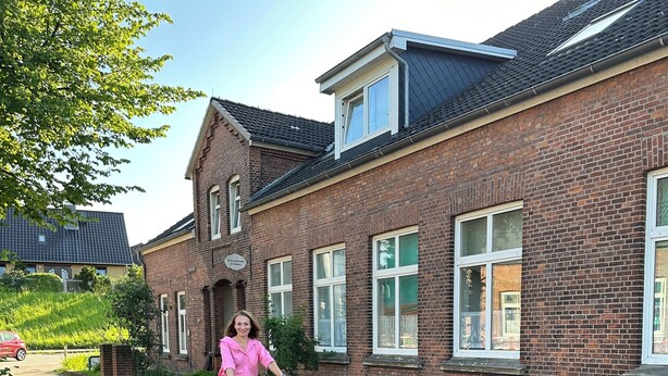 A person riding a bicycle on a brick pathway beside a brick building with multiple windows and a sloped roof. - Vacation apartment Molly (Brunsbüttel)