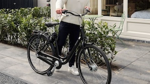 A person standing next to a bicycle on a sidewalk in front of a building with large windows and a brick facade. - Novallure Villa Margaretha (Rijswijk)