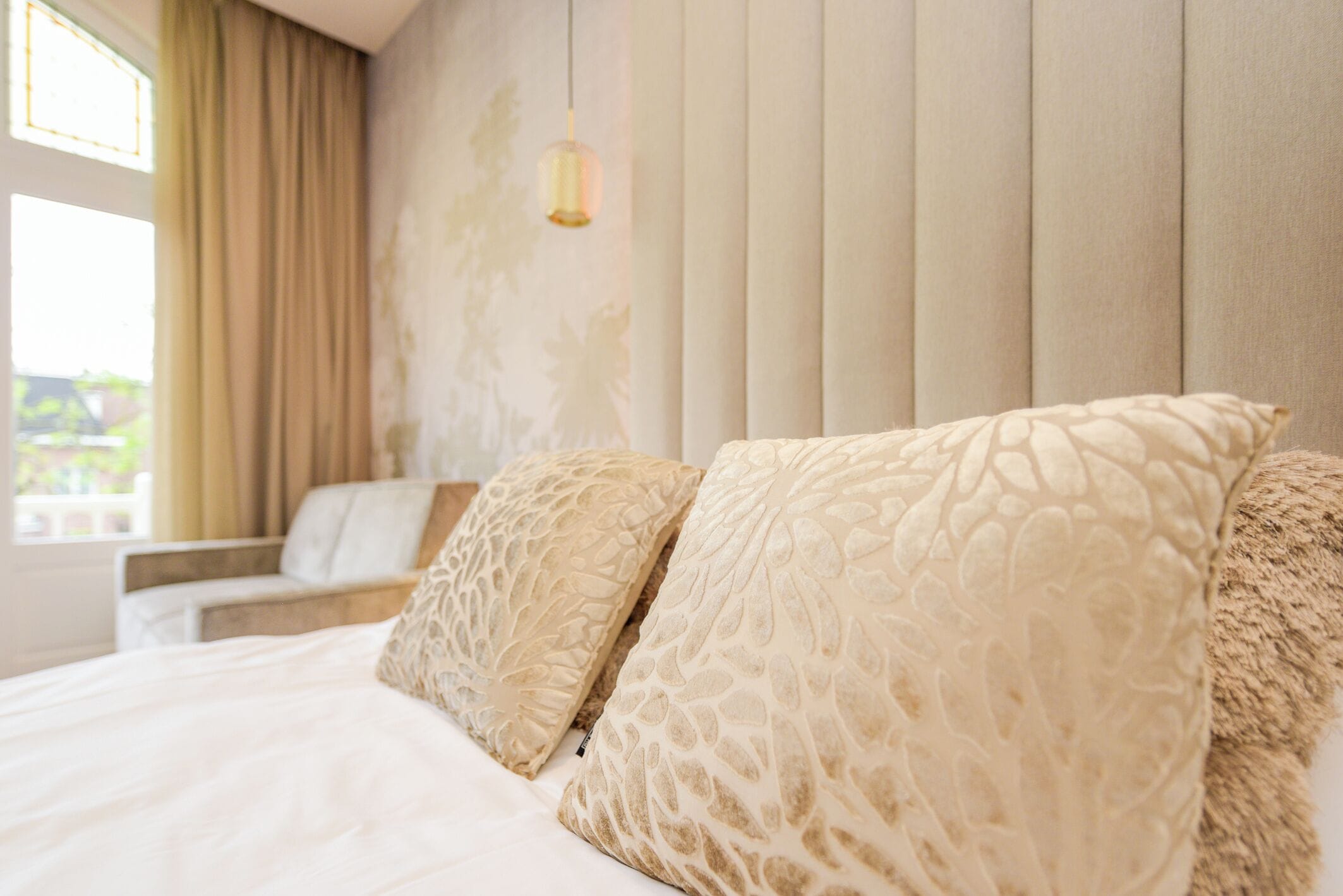 A bedroom with a bed, two pillows, a chair, and a hanging light fixture.