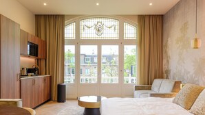 A modern hotel room with a large bed, a round coffee table, a sofa, and a kitchen area. - Novallure Villa Margaretha (Rijswijk)