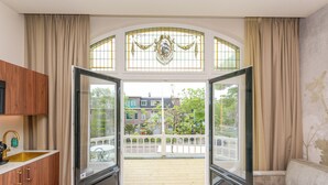 A room with a large bay window, a wooden cabinet, and a view of a balcony with a railing. - Novallure Villa Margaretha (Rijswijk)