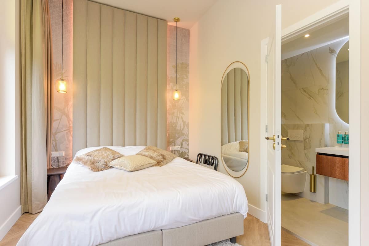 Un dormitorio con cama, lámparas de noche, un espejo y vistas al baño.