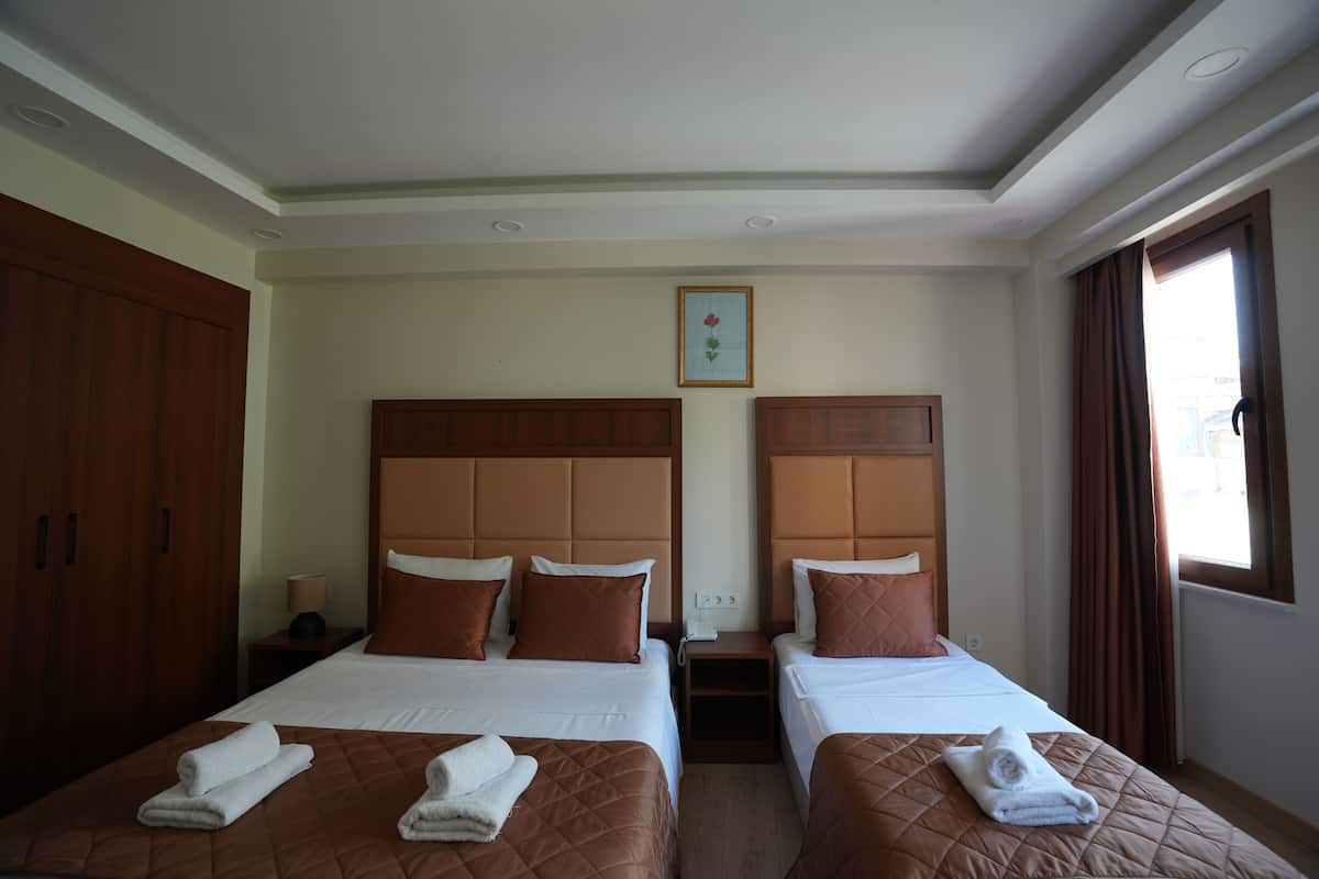 A hotel room with two beds, each with a brown quilted bedspread and white linens. There is a wooden wardrobe on the left, a nightstand with a lamp, and a framed picture on the wall.