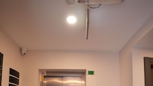 En elevator med et digitalt kontrolpanel, en røgalarm og en brandalarm på væggen.