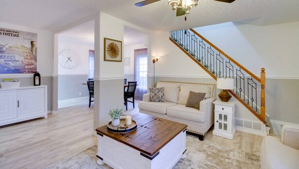 A spacious living room with a wooden coffee table, a white sofa, and a staircase with a wooden railing.