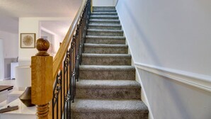 A carpeted staircase with a wooden handrail and black balusters, leading to an upper floor.