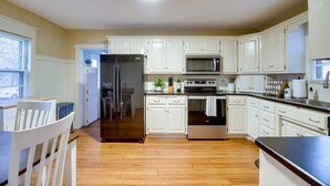 A modern kitchen with white cabinets, stainless steel appliances, and a wooden floor.