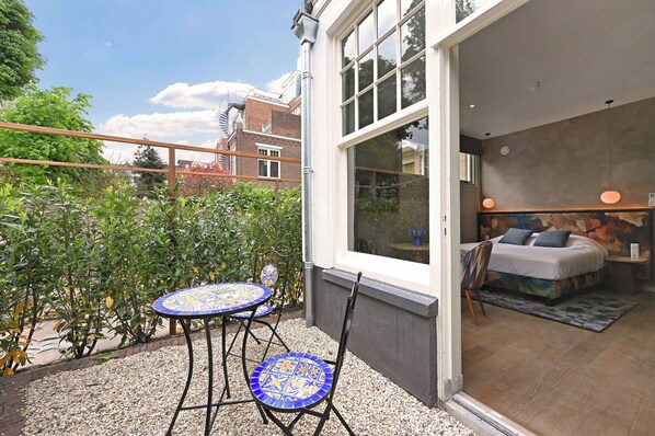 A balcony with a table and chairs, a bed with pillows, and a view of the city.