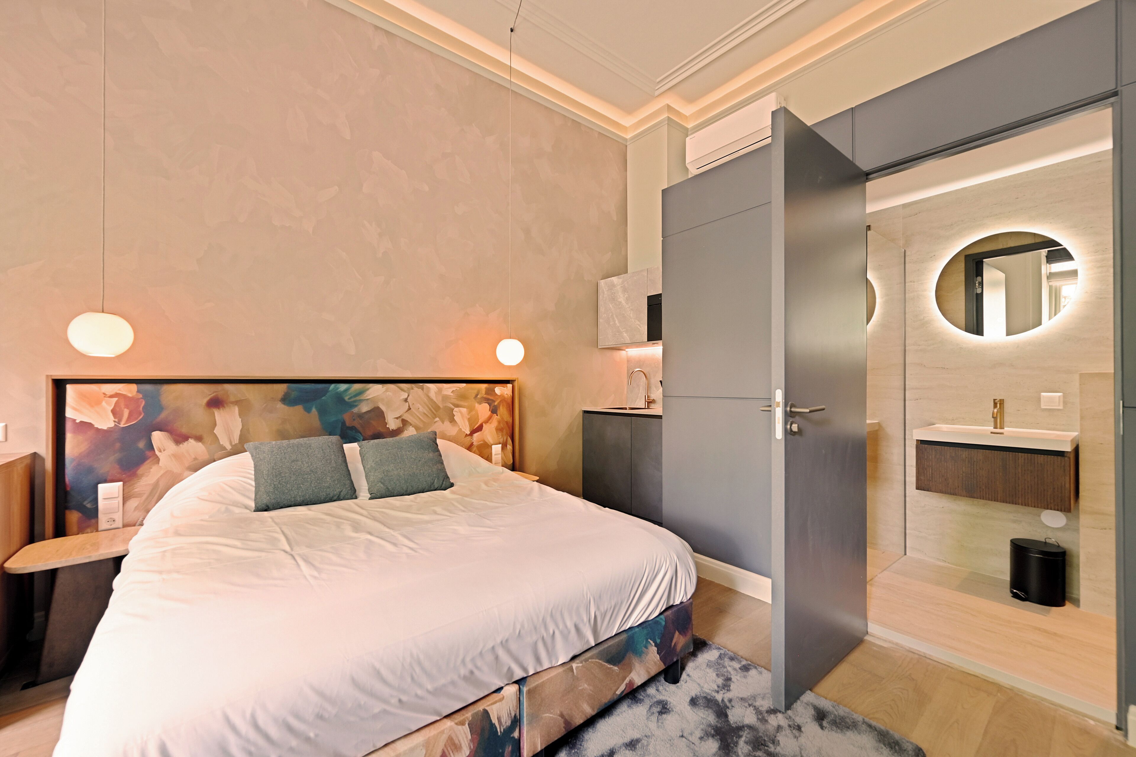 A modern bedroom with a large bed, a nightstand, a dresser, and a bathroom with a mirror and sink.